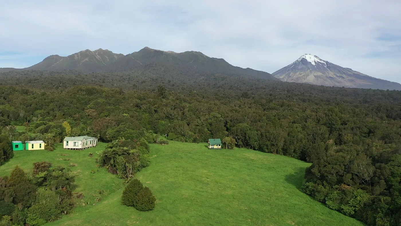 Drone view over green paddocks and native bush towards the Pouakai Range and Taranaki Maunga, near Okato